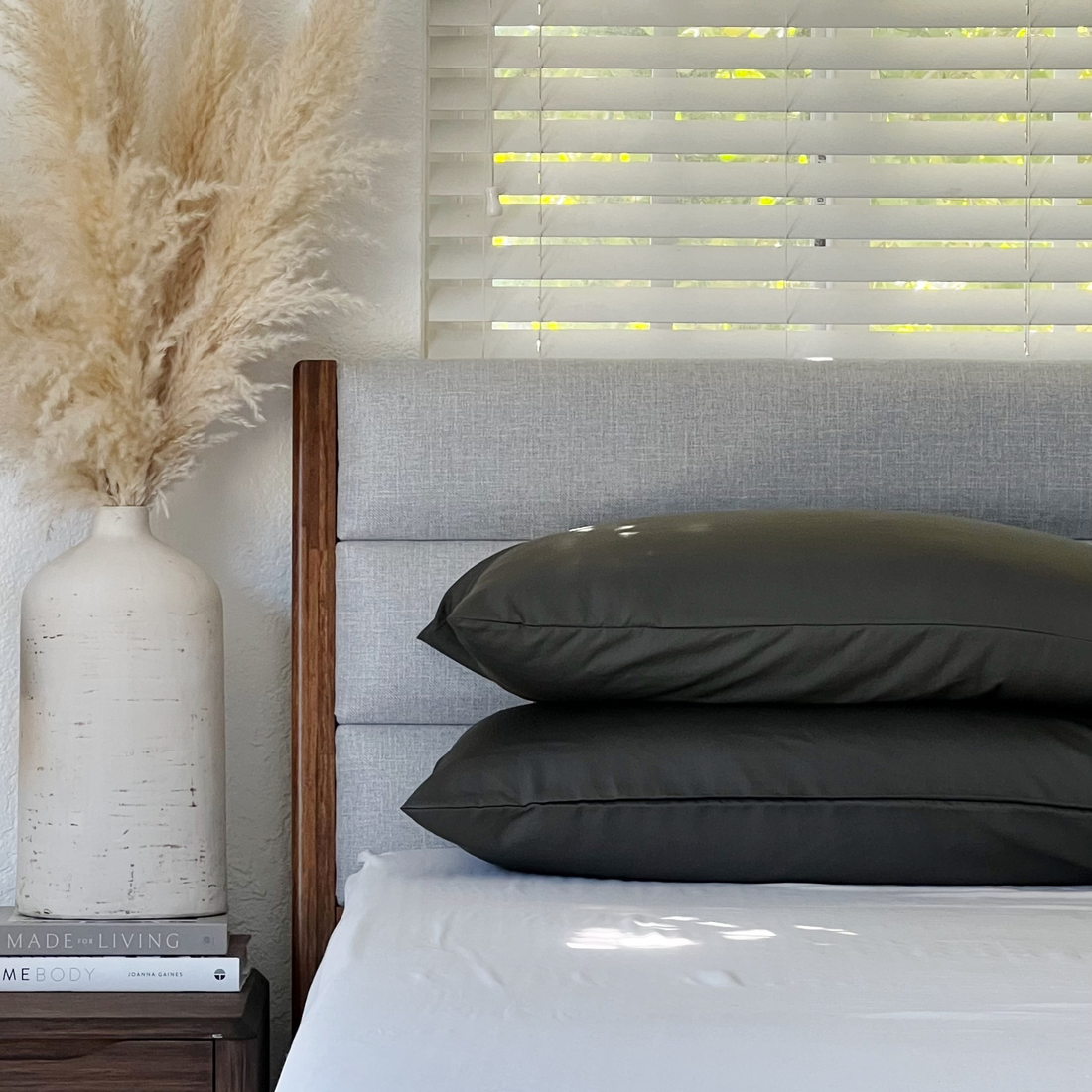 Dark grey Copper Infused Bamboo Pillowcases stacked on a bed with a grey headboard and white blinds.