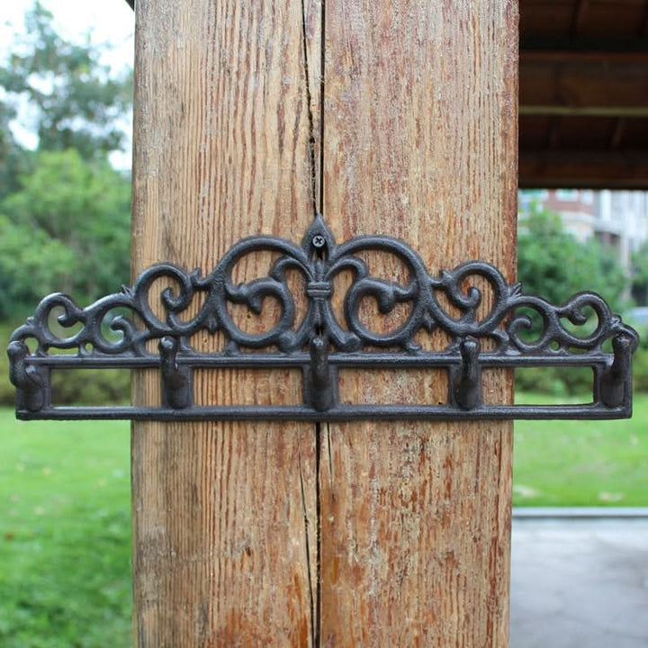 Black cast iron outdoor wall hanger with ornate scrollwork and five hooks, mounted on a wooden post.