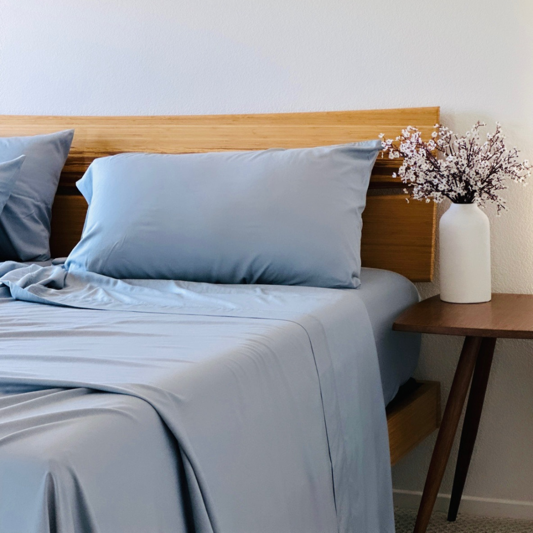 Light blue Copper Infused Bamboo Pillowcase Set on a wooden headboard, with flowers in a vase.