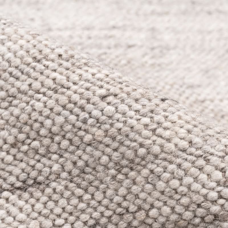 Close-up of natural wool carpet in light grey, showcasing its textured weave.