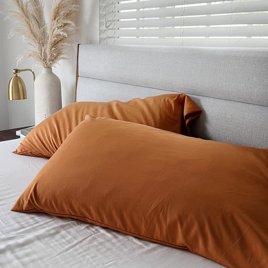 Copper Infused Bamboo Pillowcase Set in burnt orange on a white bed with grey headboard.