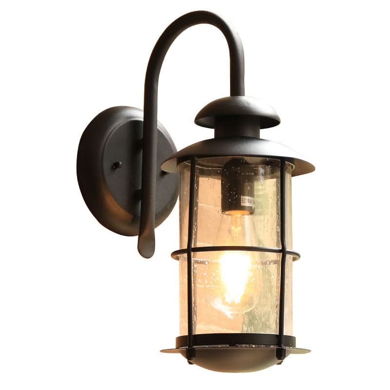 Black cylindrical outdoor sconce with seeded glass and warm Edison bulb.