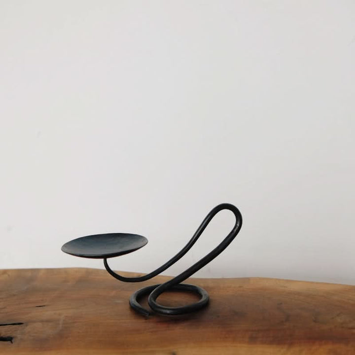 Stylish black candle holder with a unique coiled metal design, displayed on a wooden surface.