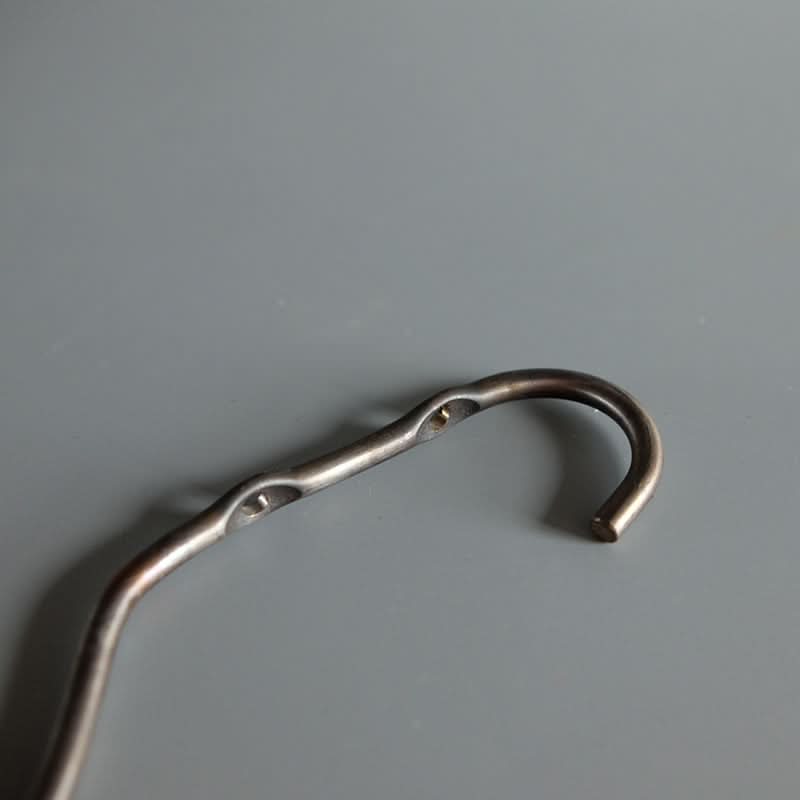 Close-up of a dark gray metal industrial style wall hook with two small screw holes on a plain gray background.