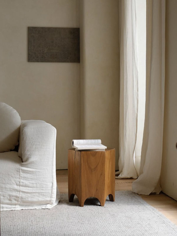 Minimalist wooden hexagonal side table with book on top, beside a white sofa.