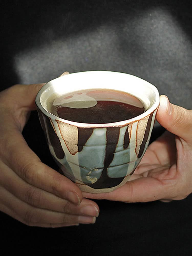 Hand-painted tea cups with autumn/winter glaze, warm earth tones, ceramic, held by hands.