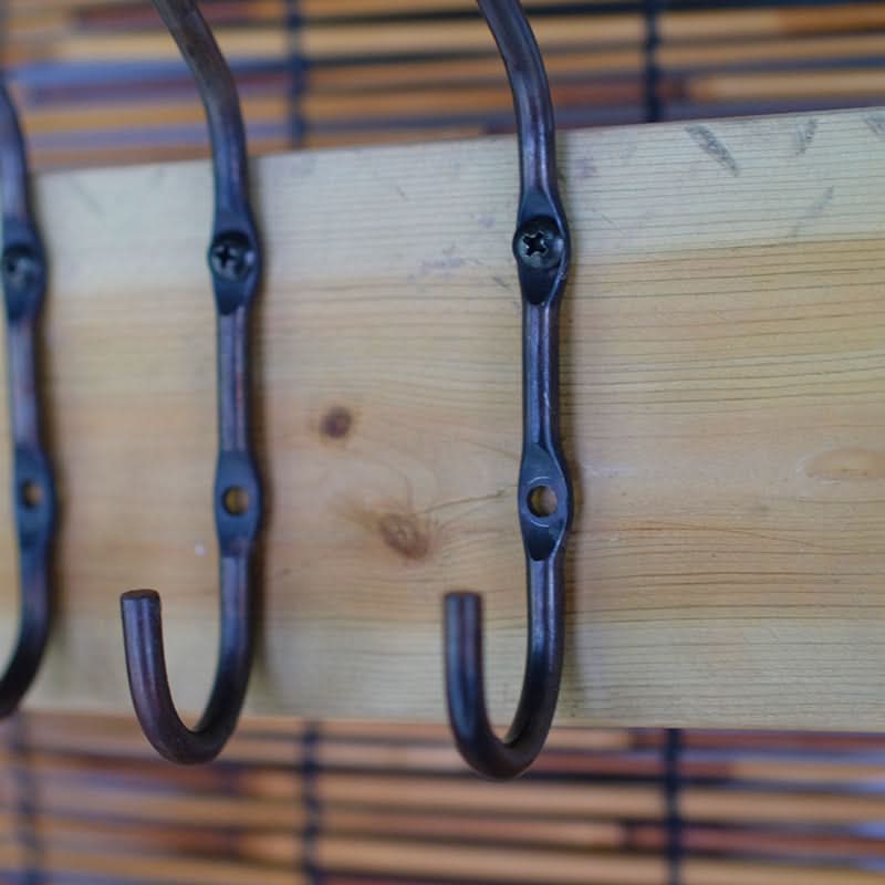 Rustic Wall Hooks - Hand forged dark iron hooks on natural wood plank, with bamboo blind background.