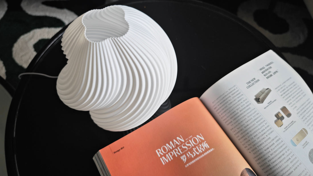 White Whimsical Wave Table Lamp with modern design on a black table next to an open magazine.