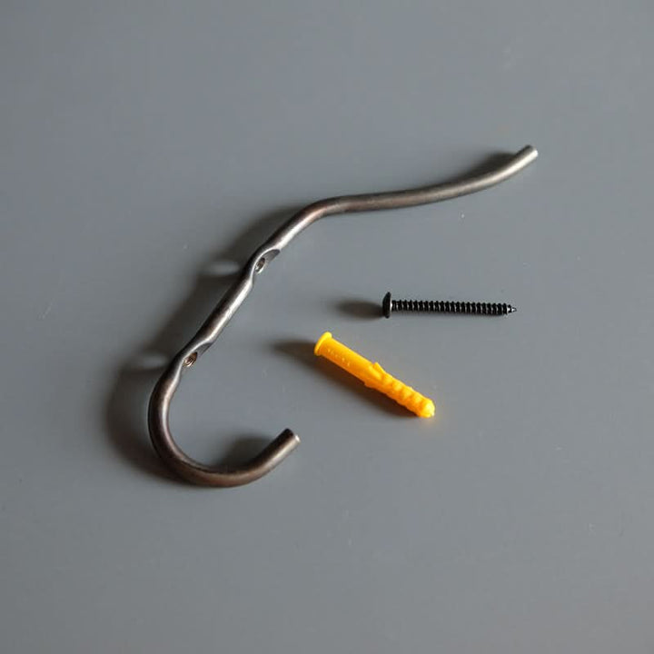 Industrial style wall hook in dark metal with screw and yellow wall plug on gray background