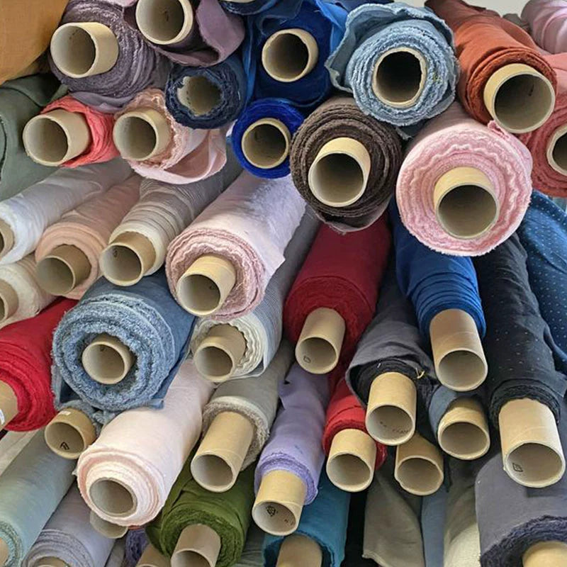 Rolls of natural linen bedding in various colors: pink, blue, red, grey, and brown.