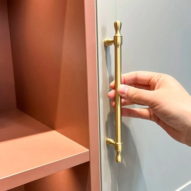 Golden brass modern extended cabinet handles shown on gray cabinet doors next to rose shelves.