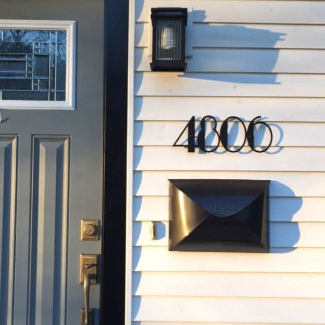 Black Mid Century Address Numbers "4800" mounted on white siding next to a gray door.