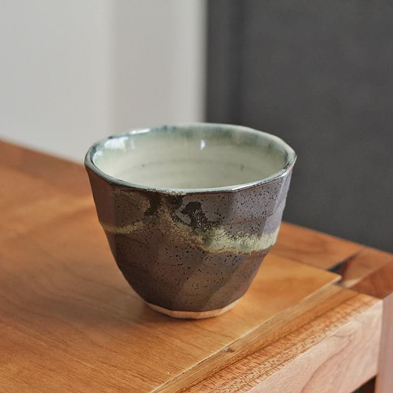 Textured ceramic Hand-Painted Tea Cup in brown and green, on a wooden surface.