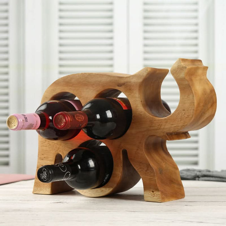Rustic wooden Thai elephant wine rack holding red wine bottles on a light wood surface.