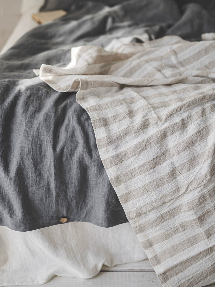 Striped linen tablecloth in beige and white, draped over a dark grey linen duvet.