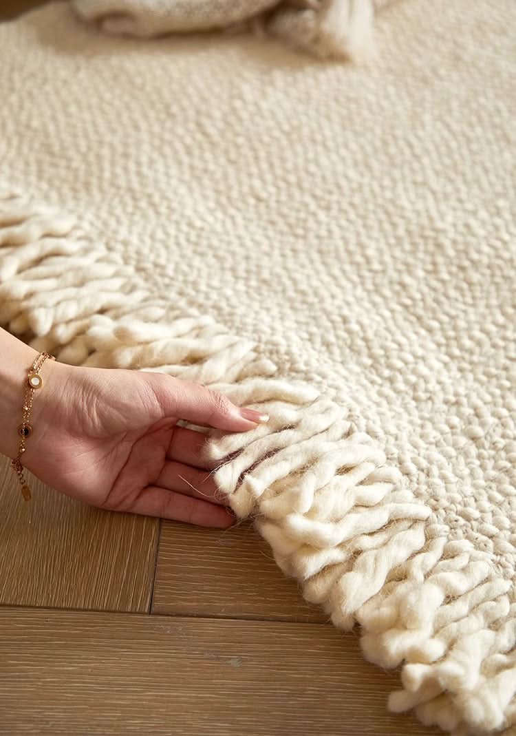 Cream braided wool rug with fringe detail on wooden floor.