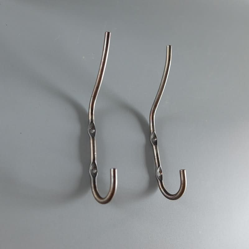 Two antique brass industrial style wall hooks on a gray background.