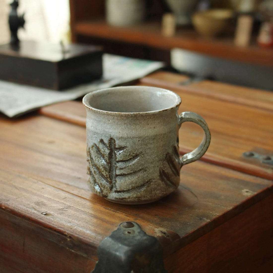 Rustic handmade ceramic coffee mug with leaf design on a vintage wooden surface.