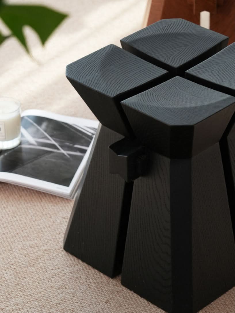 Modern geometric wooden stool in black, showcasing wood grain texture on a neutral rug.