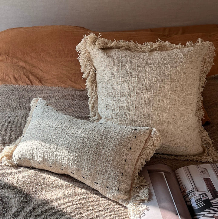 Beige woven throw pillows with fringes on a bed - set of 2