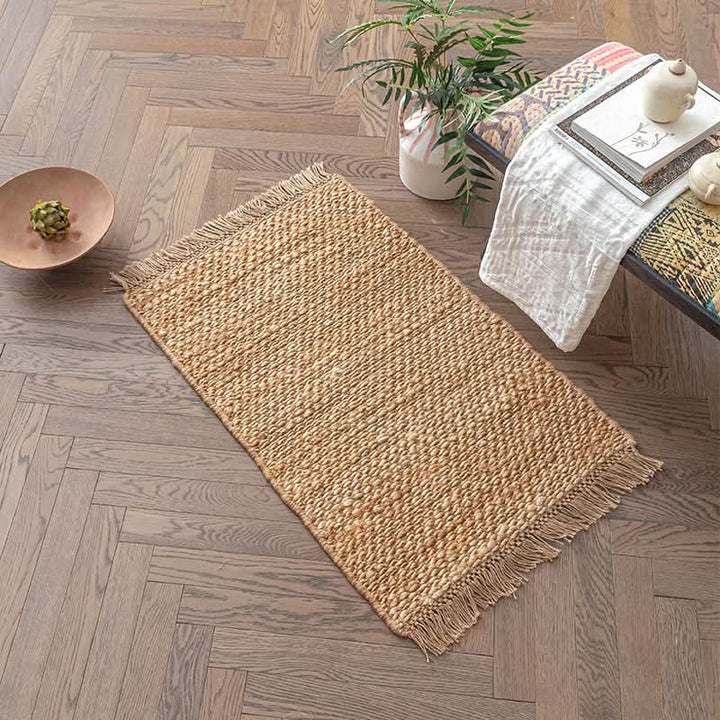 Natural woven jute area rug with fringe, styled in a modern living space with plant and books.
