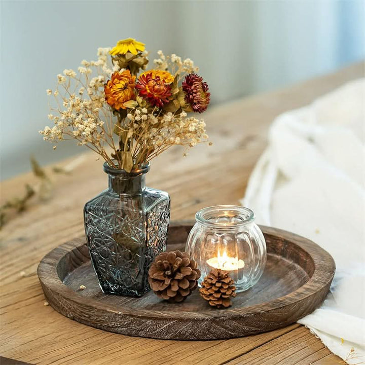 Rustic wooden tray decorative with dried flowers, candle, and pinecones on a table.