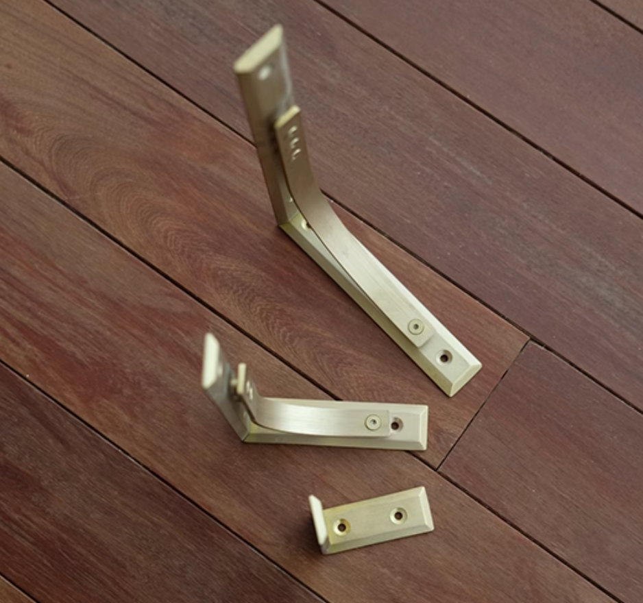 Three brushed brass shelf brackets on a dark wood background.