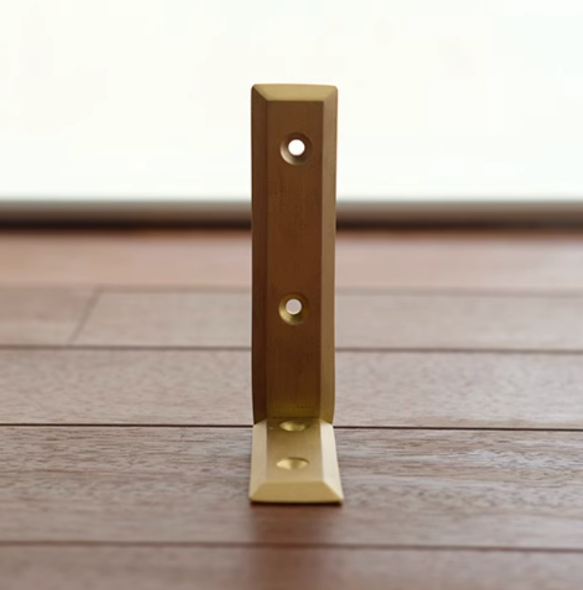 Solid brass shelf bracket with mounting holes, set on a wooden surface.