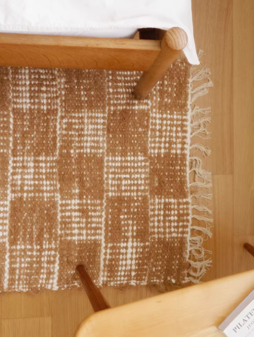 Handwoven cotton checkered rug 2.3x4.6 in brown and white, with fringed edges, near a bed and chair.