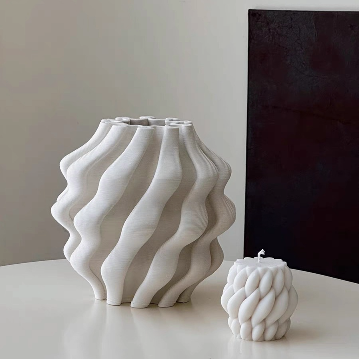 White 3D Printed Vase For Plants with wavy texture and a matching candle on a table.