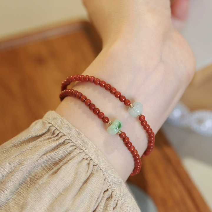 Jade bracelet with red beads and small jade accents on a wrist wearing a beige linen shirt.