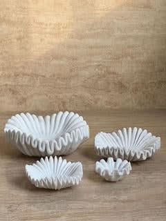 White carved marble fruit bowl set on a textured wooden surface.