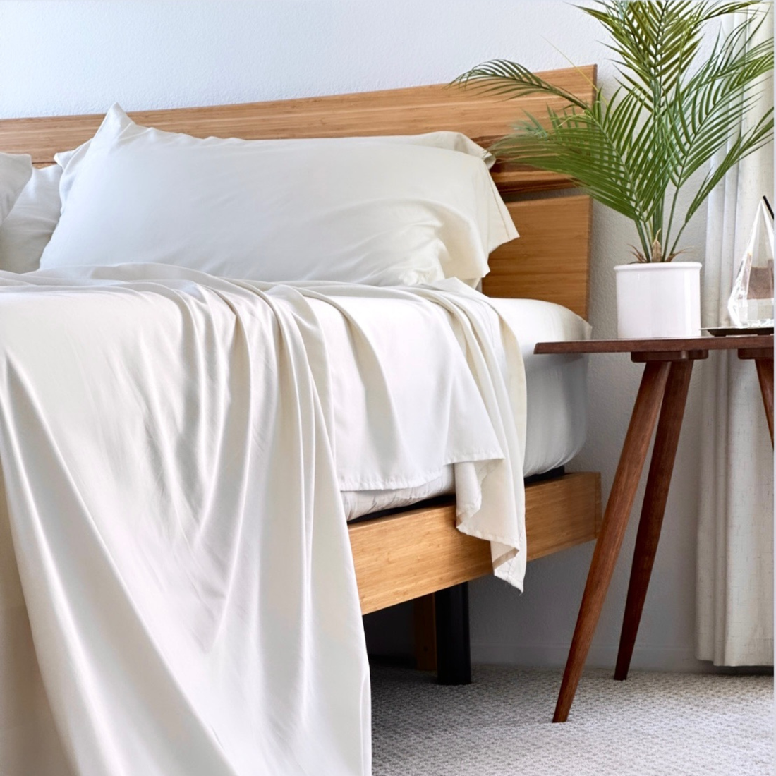 Creamy white Copper Infused Bamboo Pillowcase Set draped on a bed with wooden headboard.