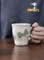 Hand-painted daisy floral mug from Pottery Japan. White ceramic with green floral design.