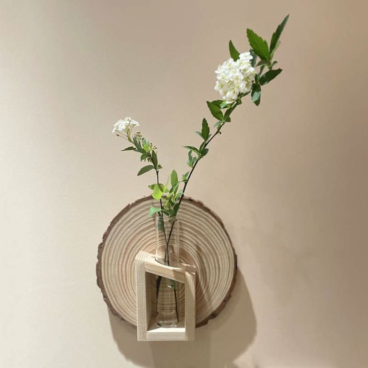 Natural wood Wall Plant Hanger Tree Ring with glass vase holding white flowers.