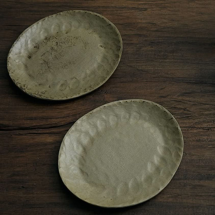 Unglazed ceramic plates with cloth texture in earthy tones on dark wood.