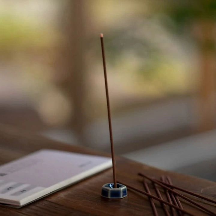 Blue ceramic incense holder made in Japan, with burning incense stick and extra sticks on table.