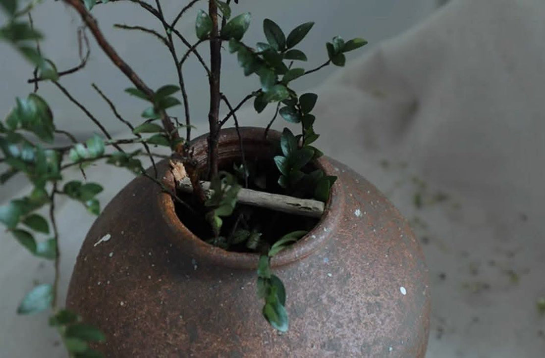 Danish-style rough earthenware vase with green branches and leaves, on textured background.