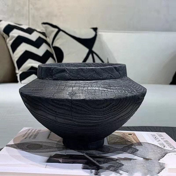 Dark wood handmade black bowl on table with decorative pillows and book.