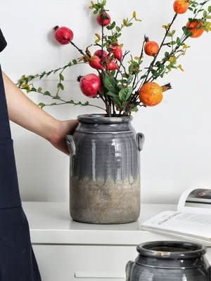 Gray stoneware double-eared vase holding dried flowers and fruit. Home decor accent.