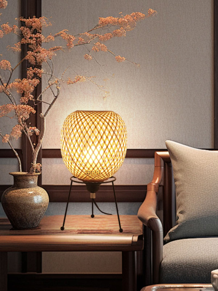 Natural rattan table lamp with woven diamond pattern and warm glow, sits on wooden table.