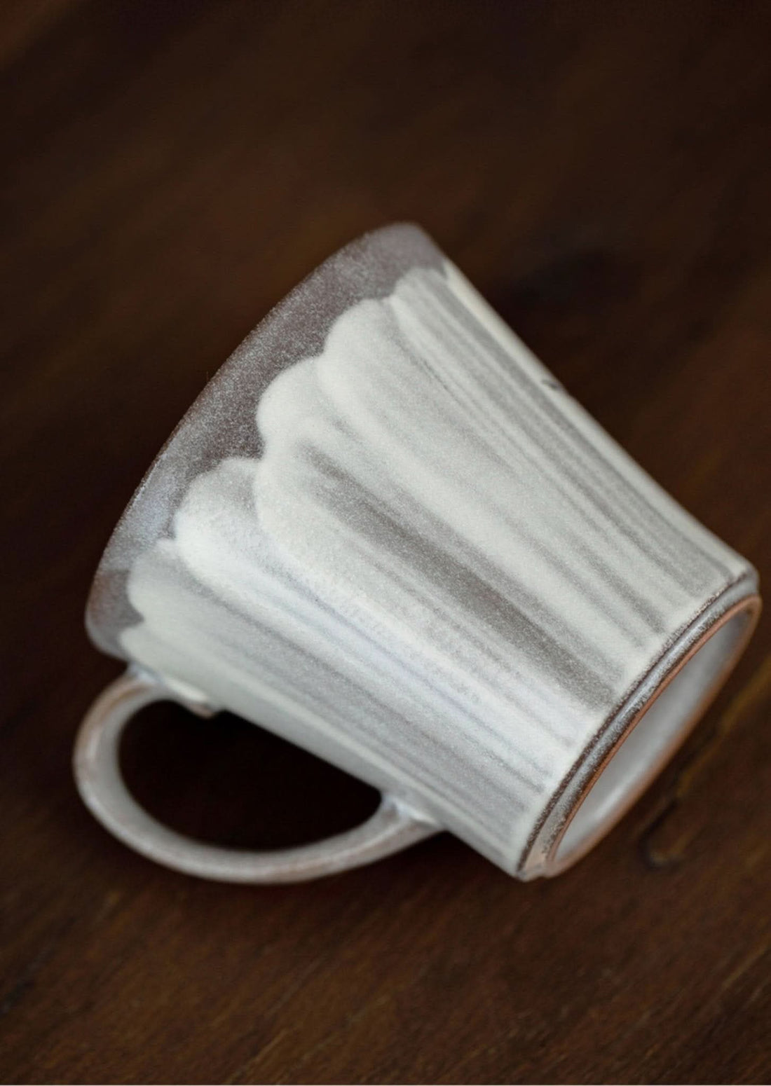 Hand-made ceramic mug with a white and grey glaze, featuring a rustic, glazed finish on a wooden surface.
