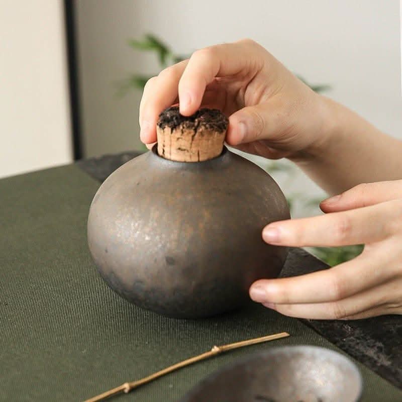 Retro ceramic tea jar with cork stopper, hands placing lid on dark textured container.