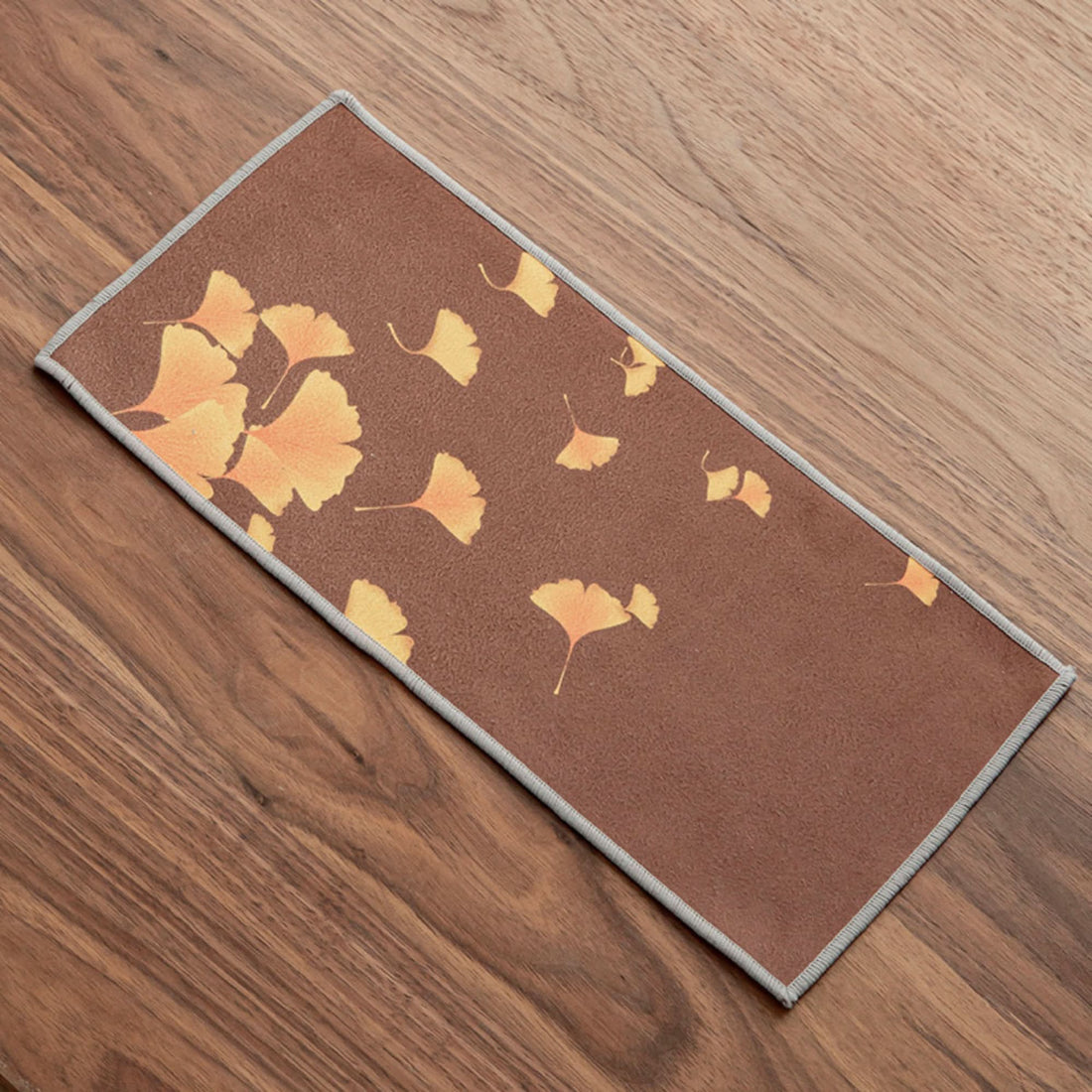 Brown Japanese tea towel with Ukiyo-e style orange ginkgo leaves, set on wood.