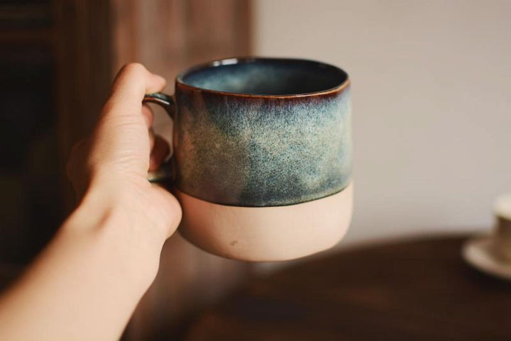 Reactive glazed pottery mug with blue-green gradient, held in hand.