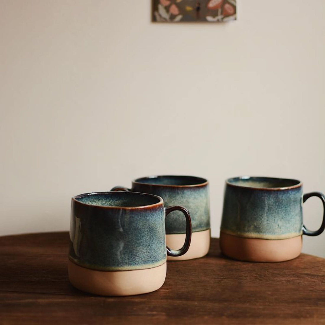 Reactive glazed pottery mugs in blue and tan, on a wooden surface.
