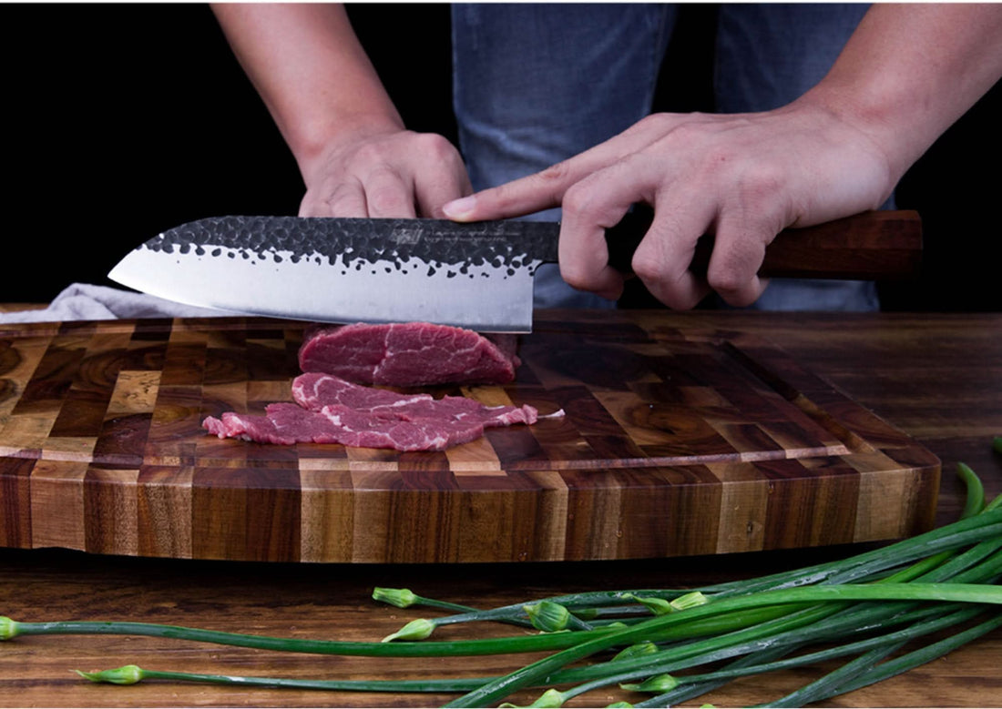 Japanese forged kitchen knife slicing raw beef on a wooden board with green onions.
