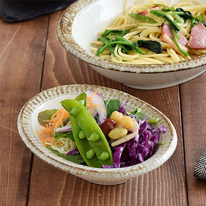 Japan imported Mino Ware beige stoneware dishes with pasta and salad on rustic wood table.