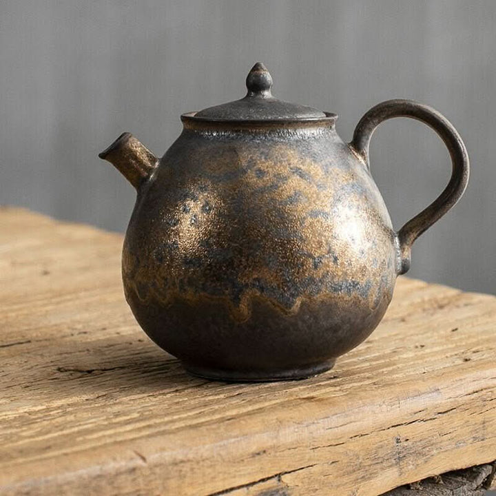 Japanese style stoneware teapot, gilt glazed, on rustic wood. Perfect tea party decor.