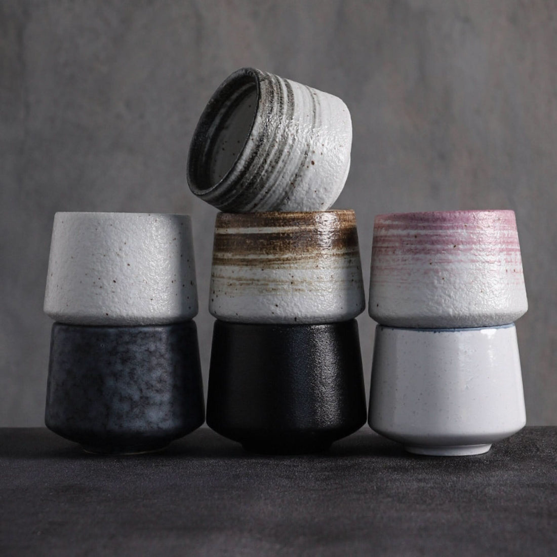 Stack of Japanese tea cups in gray tones with textured ceramic finish and varied glaze accents.